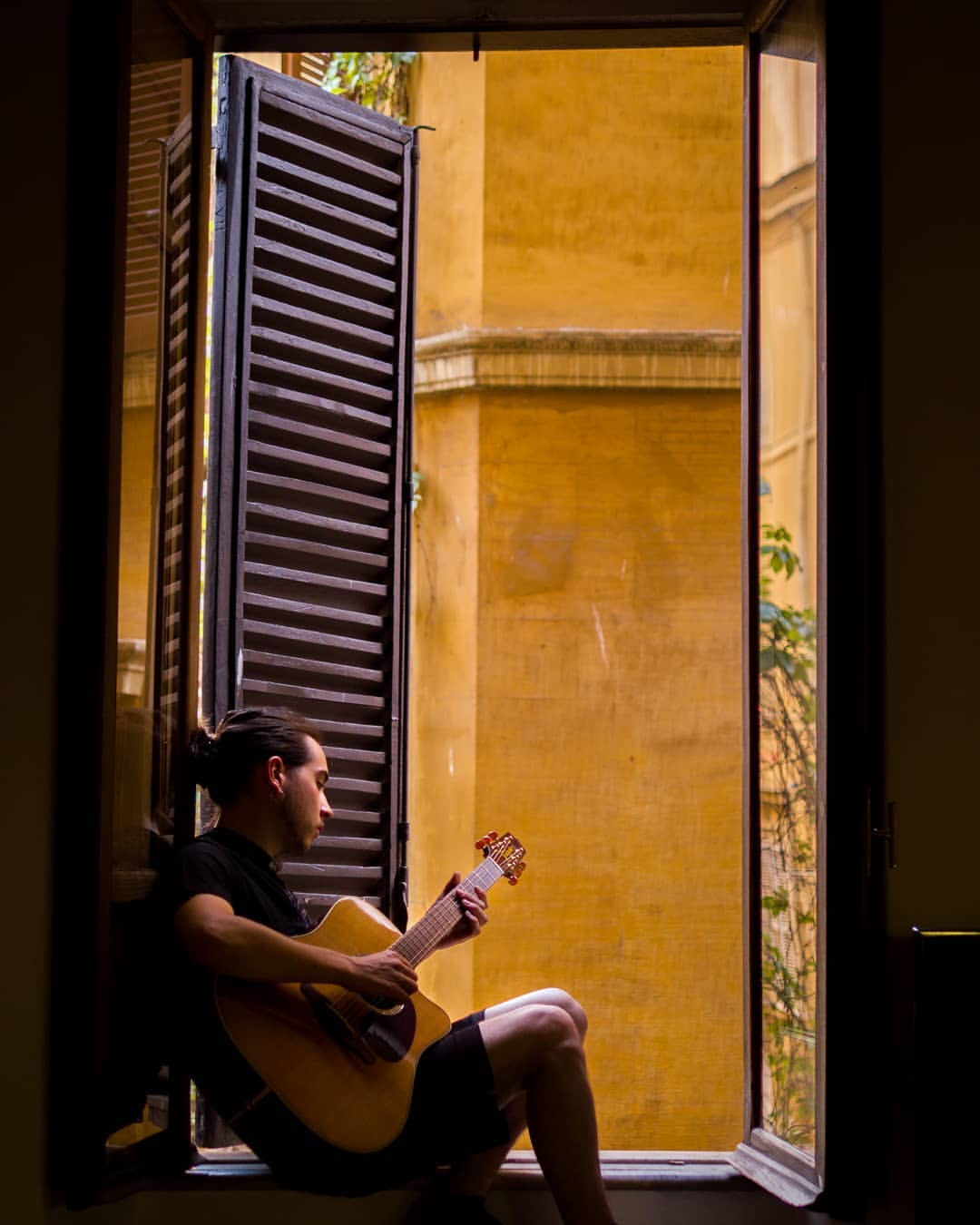 a person sitting on a window ledge playing a guitar